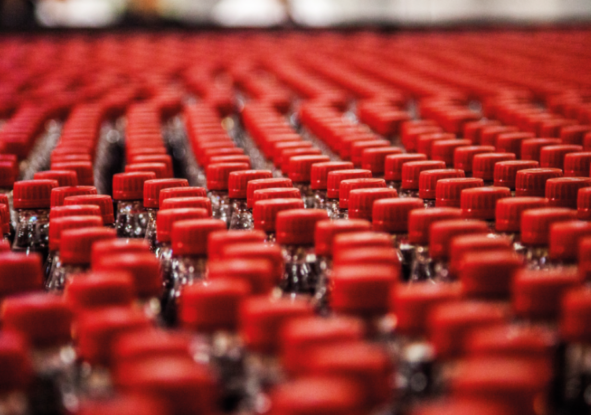 Soft drinks bottled lined up in rows with red lids