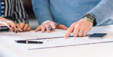 Two pairs of hands pointing at a document