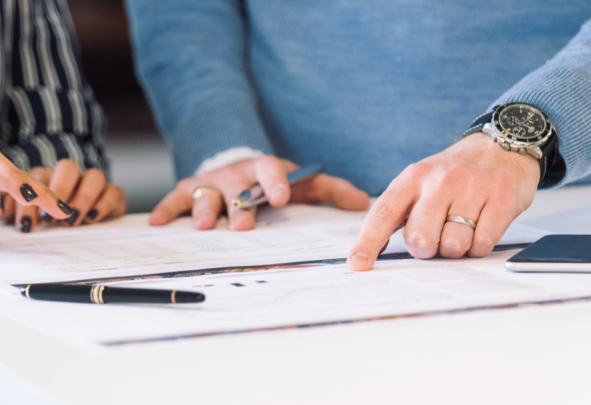 Two pairs of hands pointing at a document