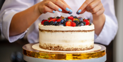 Hands seen decorating a cake with fruit