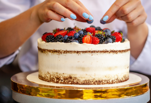 Hands seen decorating a cake with fruit