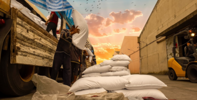 Workers unload bagges sugar from a truck against a sunset