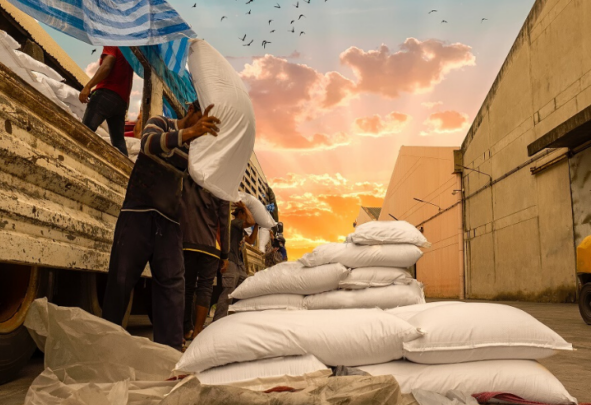 Workers unload bagges sugar from a truck against a sunset