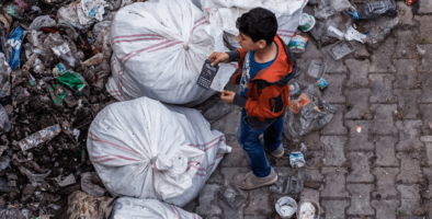 A boy stands near rubbish bags