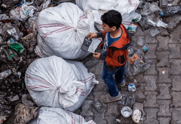 A boy stands near rubbish bags