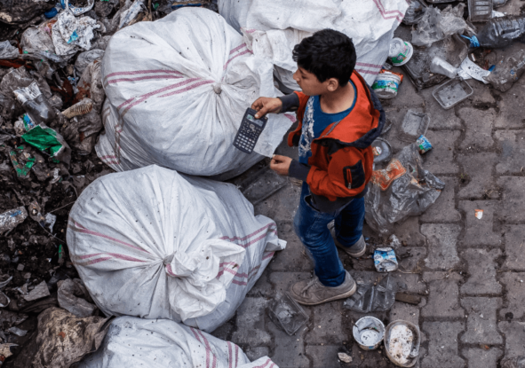 A boy stands near rubbish bags