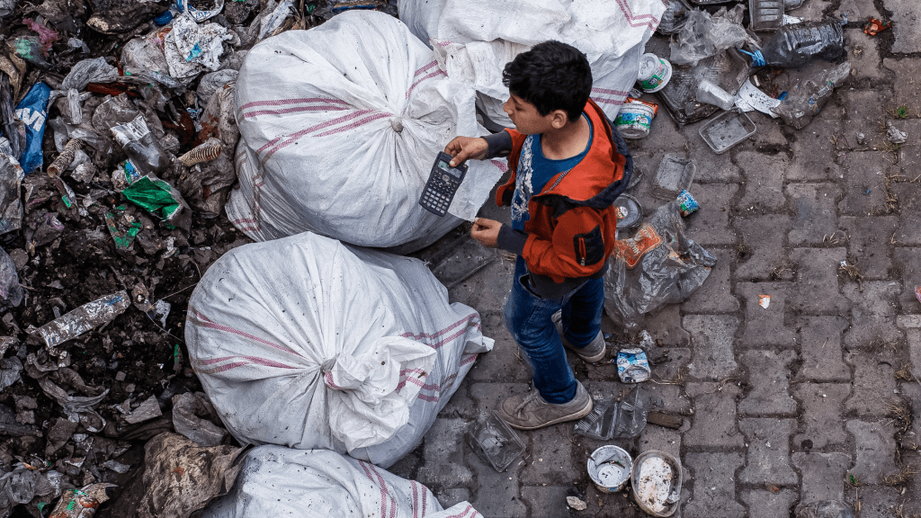 A boy stands near rubbish bags